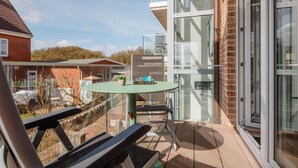 A balcony with a table and chairs, a glass door, and a view of a residential area. - Modern vacation apartment for 2 persons, new building near the beach (Juist)