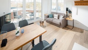 A modern living room with a wooden dining table, grey sofas, and a TV. - Welcome to the "Strandmuschel" vacation apartment - Exclusive comfort on Juist (Juist)