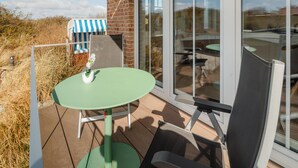A patio with a table and chairs, a striped umbrella, and a brick wall. - Welcome to the "Strandmuschel" vacation apartment - Exclusive comfort on Juist (Juist)