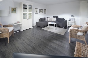 A living room with a grey sofa, wicker chairs, a white coffee table, and a cabinet with glass doors. - "Relax and feel good: Apartment Düne38 on the North Sea" (Juist)