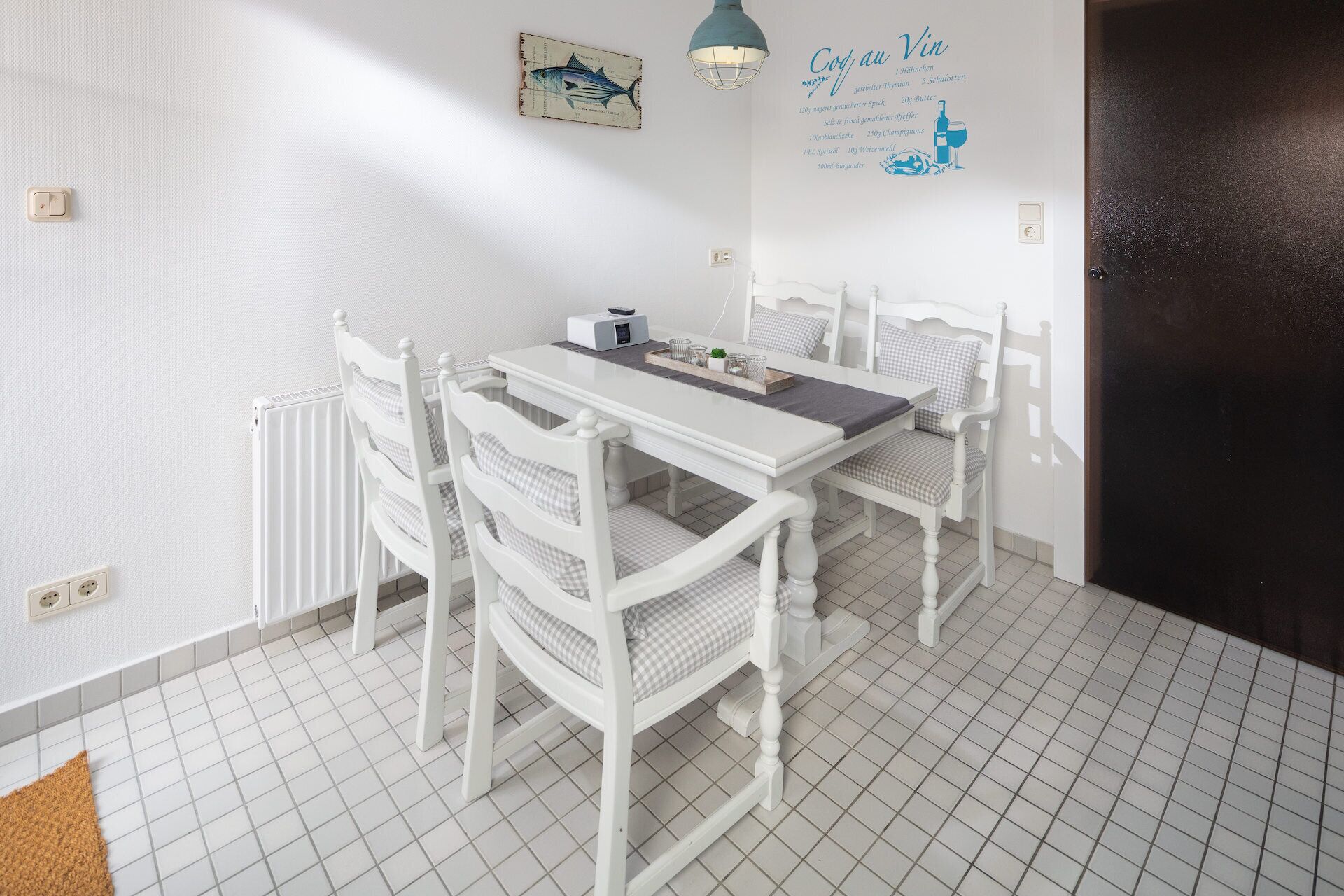 A dining area with a white table and chairs, a wall-mounted light, and a menu on the wall.