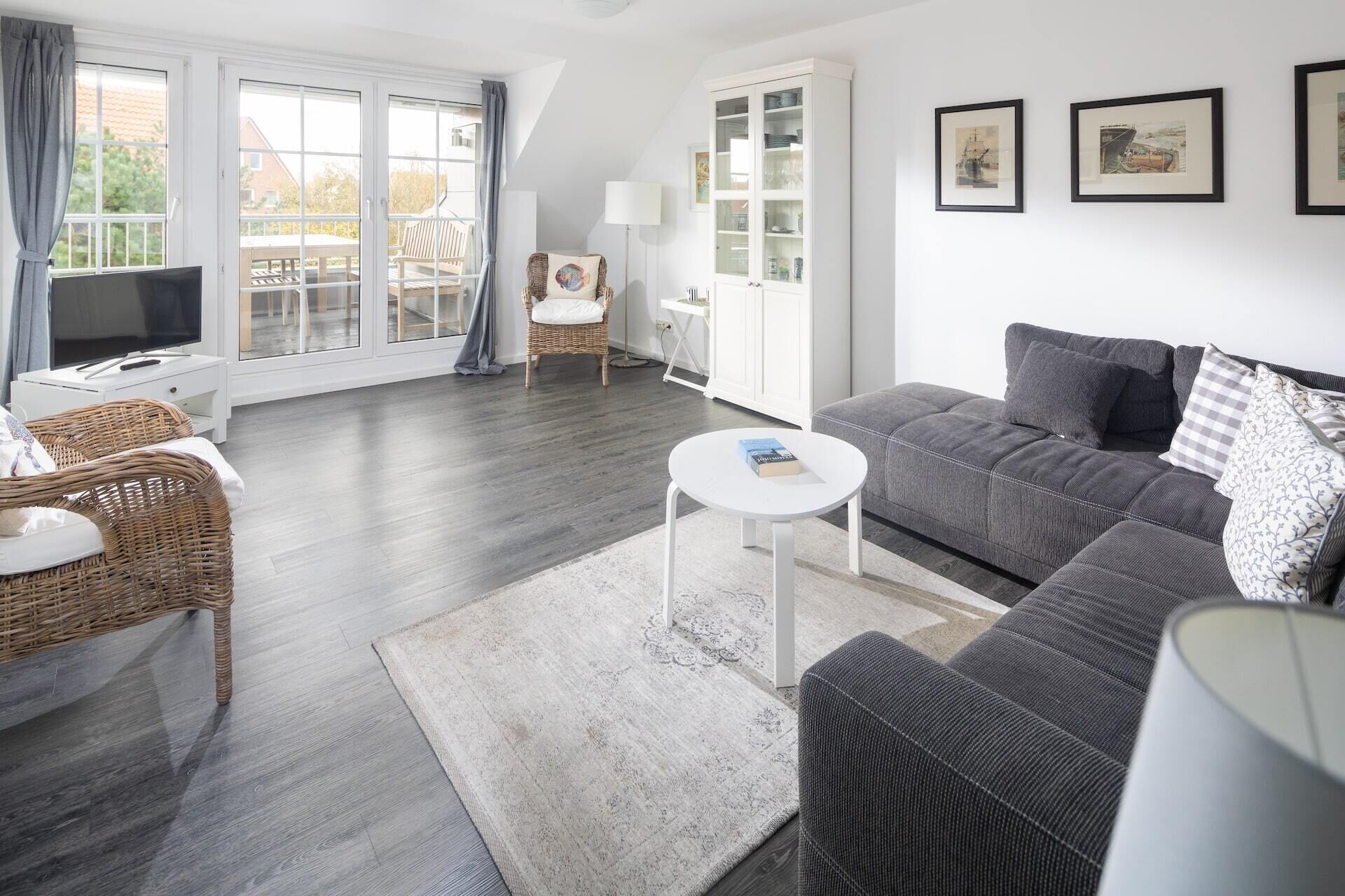 A living room with a grey sofa, wicker chairs, a white coffee table, and a flat-screen TV.