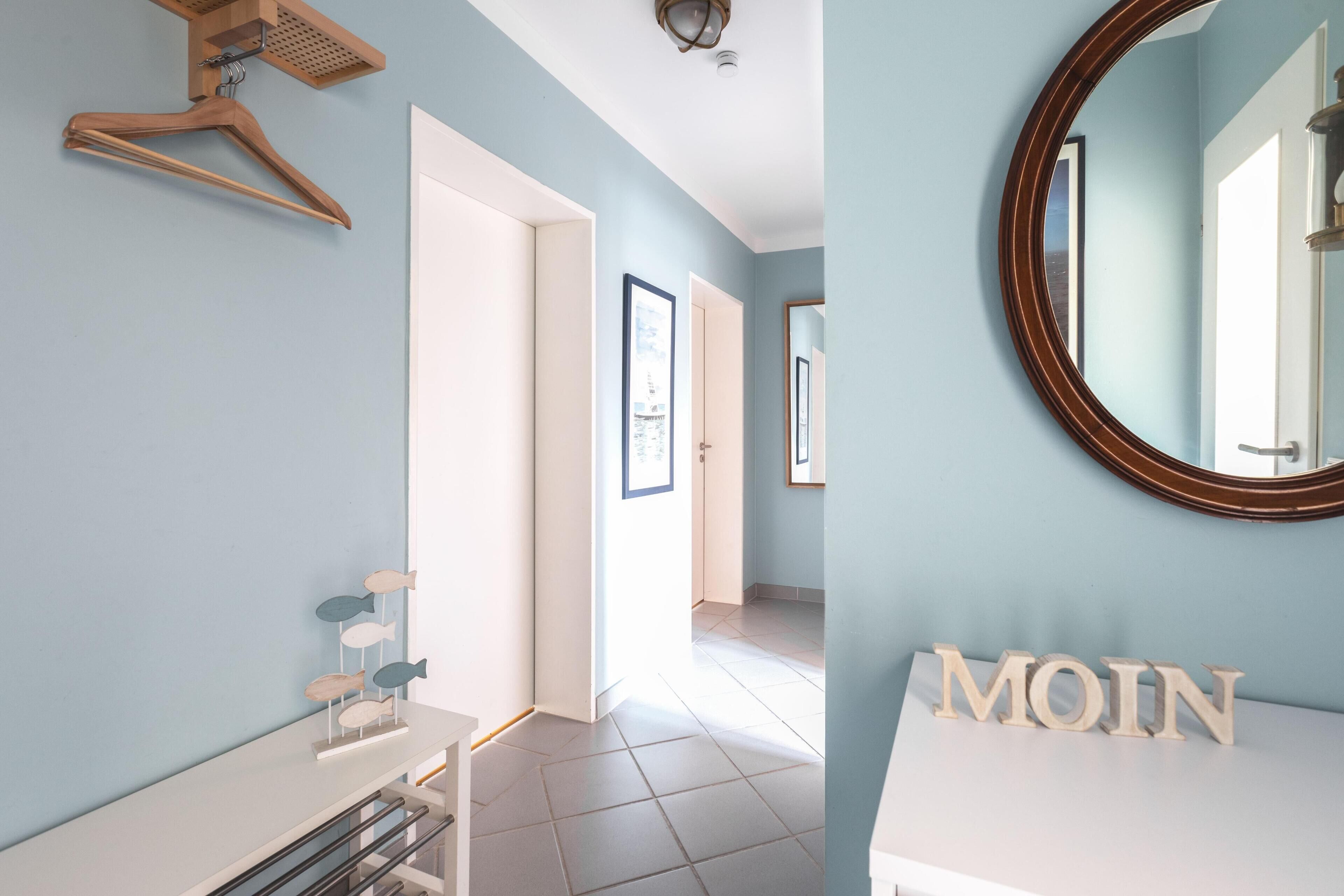A room with a light blue wall, a white door, a mirror, and a shelf with the word 'MOIN' on it.