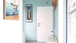 Quarto com porta branca, quadro decorativo de um farol e uma pequena estante com objetos decorativos.
