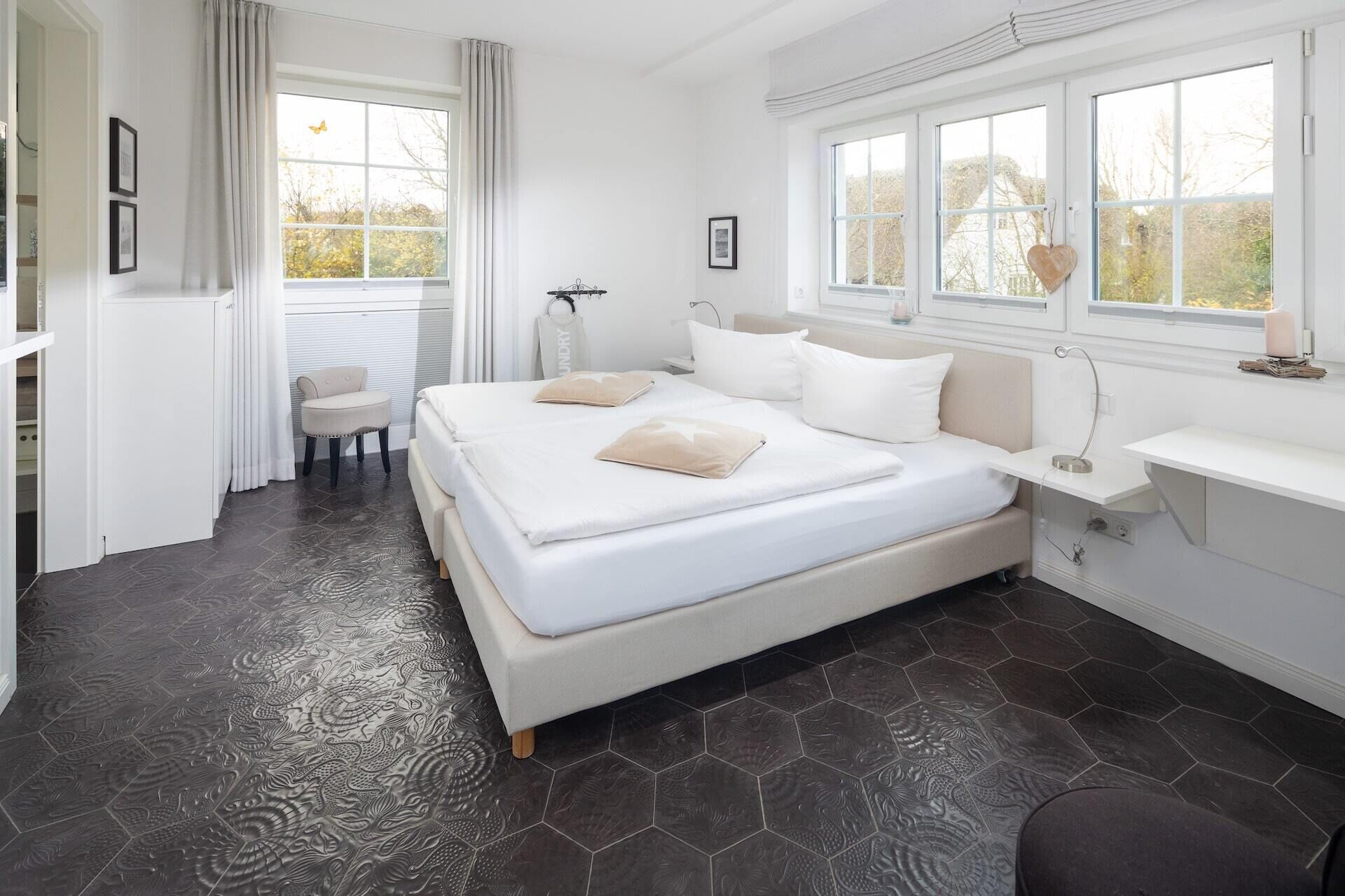 Un dormitorio moderno con una cama grande, una mesita de noche, una silla y un ventanal con cortinas.