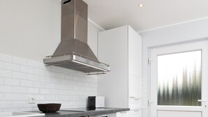Une cuisine moderne avec des meubles blancs, une hotte en acier inoxydable, un four encastré et un plancher en bois.