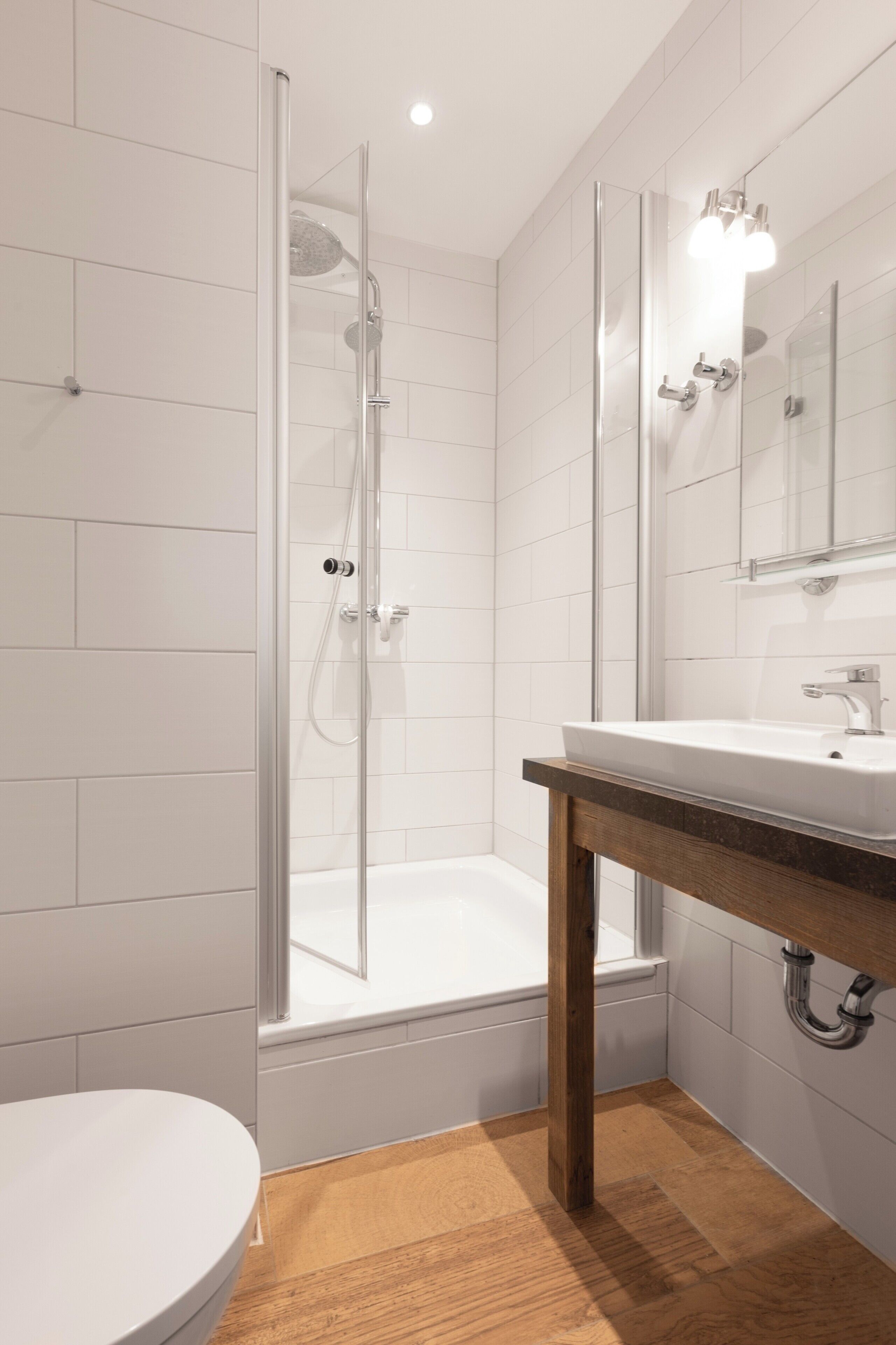 Ein modernes Badezimmer mit Duschkabine aus Glas, einem weißen Waschbecken und einem Holz-Waschtisch.