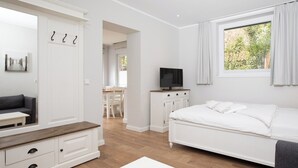 Une chambre moderne avec un lit, une télévision, une armoire blanche et un coin repas visible à travers une porte ouverte.