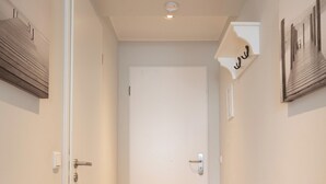 Un couloir doté d’un plancher en bois, de murs blancs et d’une porte blanche au fond.