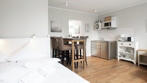Une chambre avec un grand lit, une table à manger en bois avec des chaises, une cuisine avec des meubles blancs et un four à micro-ondes.