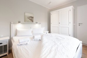 A neatly made bed with white linens, a bedside table with a lamp, and a large white wardrobe. - Apartment in a quiet location with balcony (Juist)