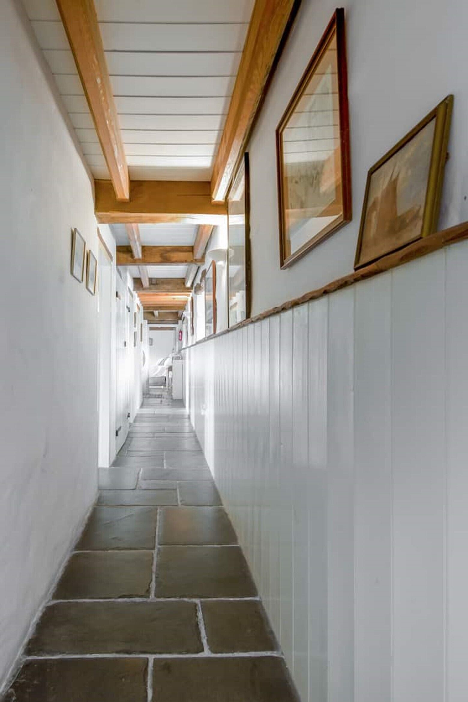 A corridor with white walls, wooden beams, and stone flooring.