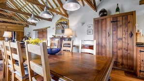 Ein rustikaler Essbereich mit Holzsesseln, einem großen Holztisch, hängenden Pendelleuchten und einem Holzkabinett.