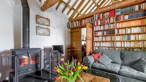 Ein gemütliches Wohnzimmer mit Kamin, einer Couch, einem Bücherregal und einer Vase mit Blumen.