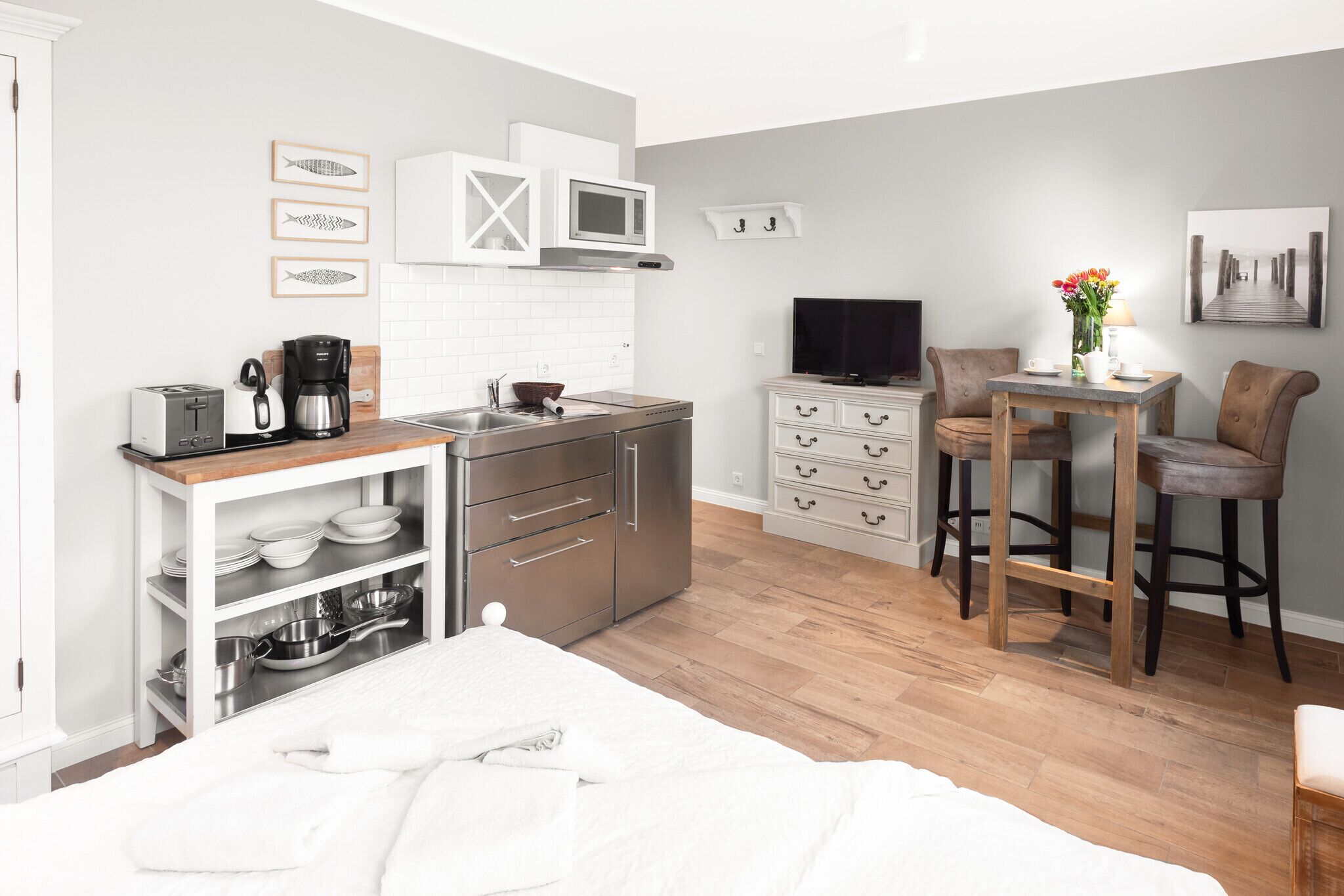 A compact kitchen with a microwave, toaster, and coffee maker, a dining area with a table and chairs, and a TV on the wall.