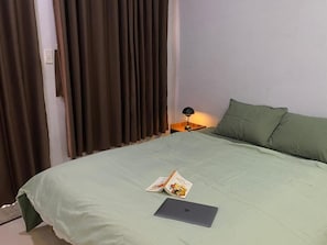 A neatly made bed with a laptop and a book on it, a bedside lamp, and a window with curtains. - Peanuts Home Calmette (Ho Chi Minh City)