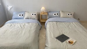 Een kamer met twee bedden, elk voorzien van een geruit sprei en passende kussens met een gezicht dessin. Daartussen staat een klein nachtkastje met een lamp. Op het bed op de voorgrond liggen een laptop en een boek.