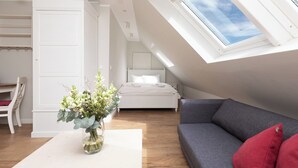Un dormitorio con tragaluz, una cama, un sofá gris y un armario blanco.