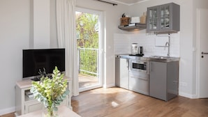 Una cocina compacta con televisor, un comedor con un florero y una puerta corrediza de vidrio que da a un espacio exterior.
