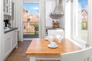 A modern kitchen with white cabinets, a wooden table, and a view of a red brick house through a glass door. - Apartment in a quiet location with balcony (Juist)
