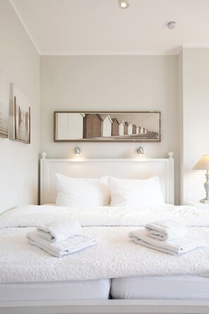 A neatly made bed with white linens and pillows, a bedside table with a lamp, and a wall-mounted artwork above the bed. - Apartment in a quiet location with balcony (Juist)