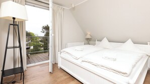 Un dormitorio con cama blanca, una lámpara de pie y vistas al exterior.