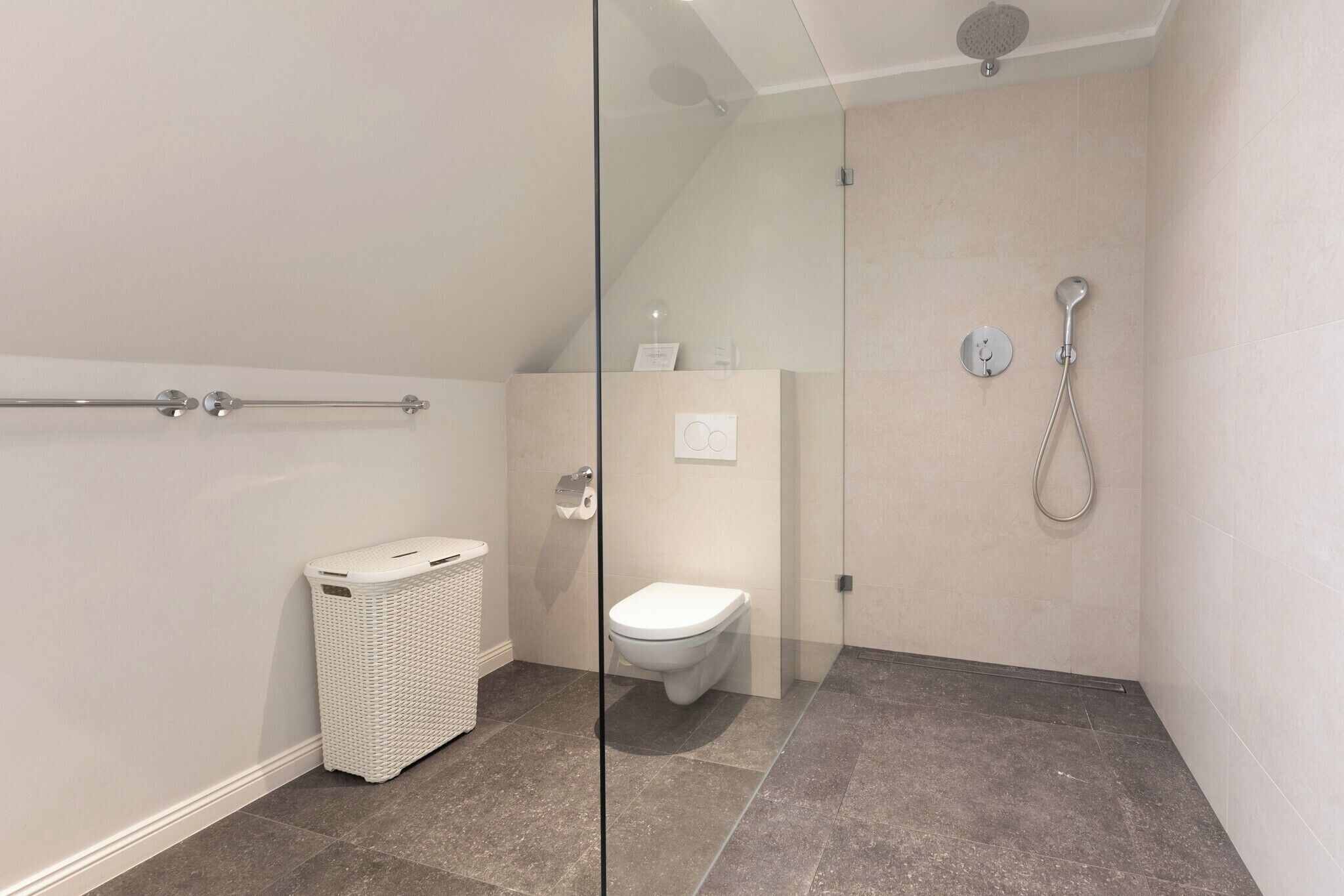 Een moderne badkamer met een douchecabine van glas, een wit toilet en een witte wasmand.