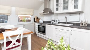 Una cocina moderna con armarios blancos, una campana extractora de acero inoxidable, un horno integrado y un ventanal con vistas a edificios.