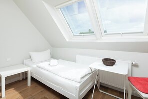 A white room with a bed, a small table, a red chair, a white radiator, and a skylight. - Vacation room in a quiet location (Juist)