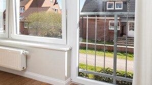 Ein Zimmer mit großen Fenstern, einem Heizkörper, einem Tisch mit zwei weißen Tassen und Blick auf ein Backsteinhhaus.