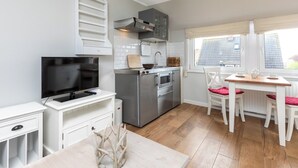Eine kompakte Küche mit Fernseher, Kühlschrank, Backofen und einem Essbereich mit Tisch und Stühlen.