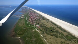 Ein Luftbild einer Küstenstadt mit Strand, grünen Feldern und einer Straße.
