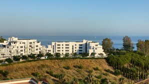 A coastal residential area with modern white buildings, a grassy hill, and a clear view of the sea. - Beach Apartment with Pool, Terrace & Parking (Velilla-Taramay)