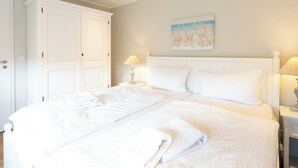 A neatly made bed with white linens, a large white wardrobe, and a beach-themed painting on the wall. - Vacation apartment in a quiet location (Juist)