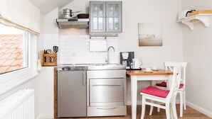 A compact kitchen with a built-in oven, a coffee maker, and a dining area with a table and chairs. - Vacation apartment in a quiet location (Juist)