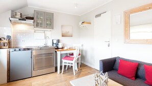 A compact kitchen with modern appliances, a dining area with two chairs, and a sofa with red cushions. - Vacation apartment in a quiet location (Juist)