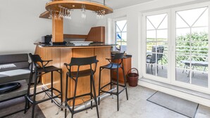 Cozinha moderna com ilha central, banquetas e uma grande janela com vista para vegetação.
