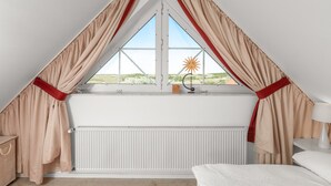 Um quarto com teto inclinado, janela com cortinas, radiador, cama e mesa de cabeceira.