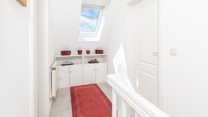 Um corredor estreito com um claraboia, paredes brancas, um tapete vermelho e uma porta branca.