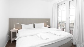 A large bed with white bedding, two bedside tables with lamps, a wooden headboard, and a view of a balcony through a glass door. - "Fantastic vacation apartment with sea view and exclusive furnishings on Juist!" (Juist)