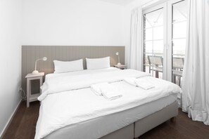 A large bed with white bedding, two bedside tables with lamps, a wooden headboard, and a view of a balcony through a glass door. - "Fantastic vacation apartment with sea view and exclusive furnishings on Juist!" (Juist)