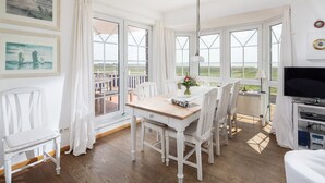 A dining area with a wooden table and white chairs, large windows with a view of the sea, and a television on a stand. - "Fantastic vacation apartment with sea view and exclusive furnishings on Juist!" (Juist)