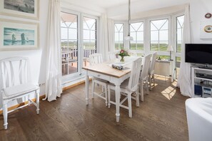 A dining area with a wooden table and white chairs, large windows with a view of the sea, and a television on a stand. - "Fantastic vacation apartment with sea view and exclusive furnishings on Juist!" (Juist)