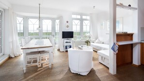 A spacious room with a wooden dining table, white sofa, and a TV. - "Fantastic vacation apartment with sea view and exclusive furnishings on Juist!" (Juist)