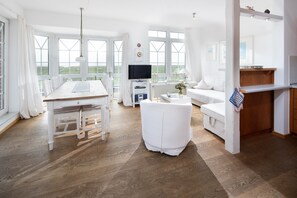 A spacious room with a wooden dining table, white sofa, and a TV. - "Fantastic vacation apartment with sea view and exclusive furnishings on Juist!" (Juist)