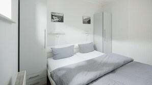 Quarto com cama, guarda-roupa, mesa de cabeceira e luminárias fixadas na parede.