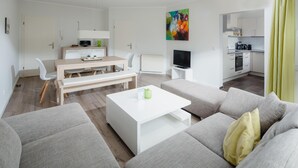 Uma sala de estar moderna com sofá, mesa de centro, televisão e uma área de refeições com cadeiras e mesa.