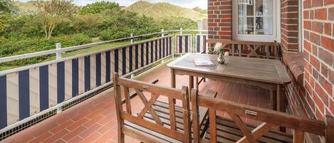 En balkon med et bord og stole, en murstensvæg og udsigt til grønne omgivelser.