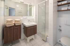 Ein Badezimmer mit Waschbecken, Spiegel, gestapelten Handtüchern, Dusche und Toilette.