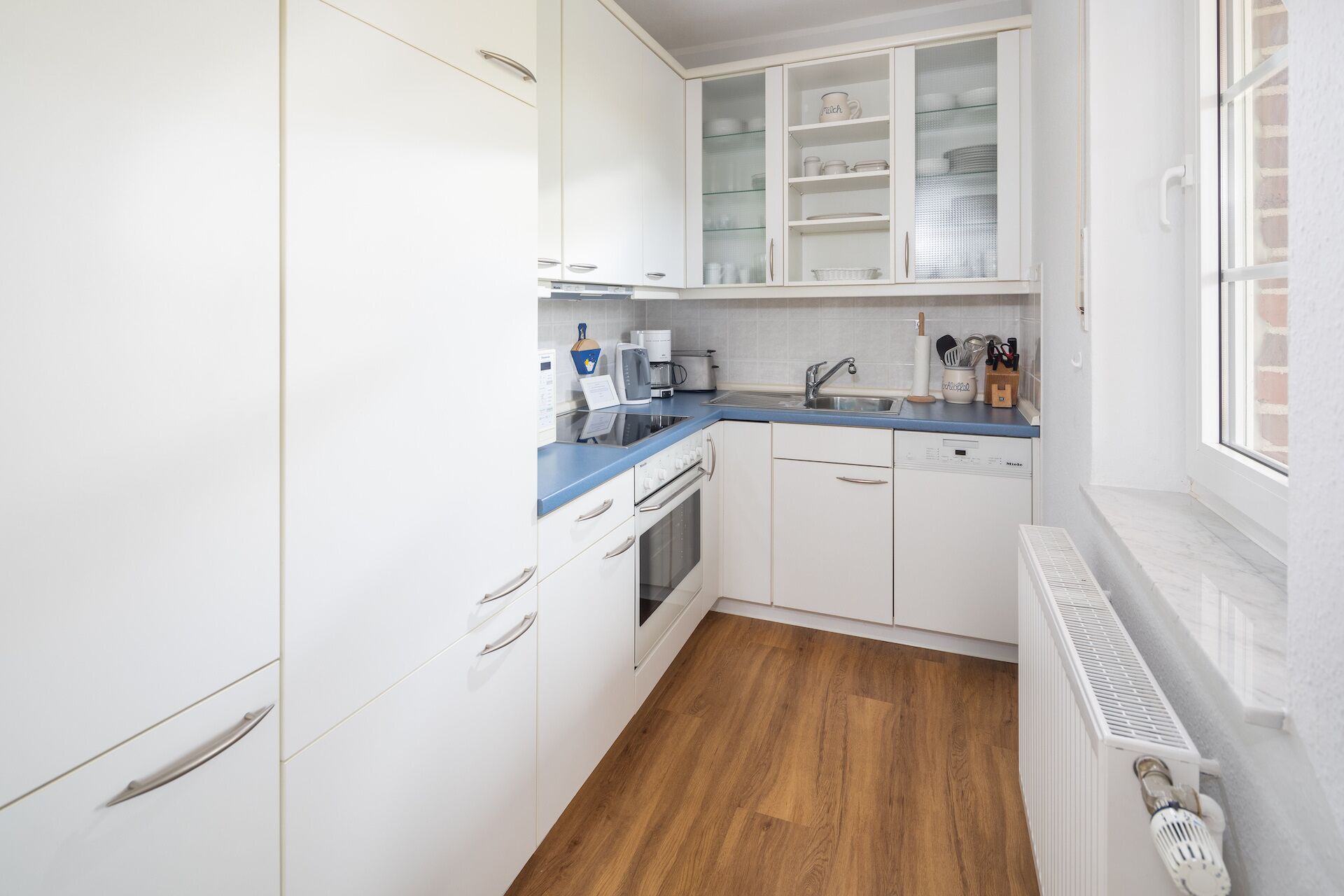 A compact kitchen with white cabinets, a blue countertop, and a built-in dishwasher.